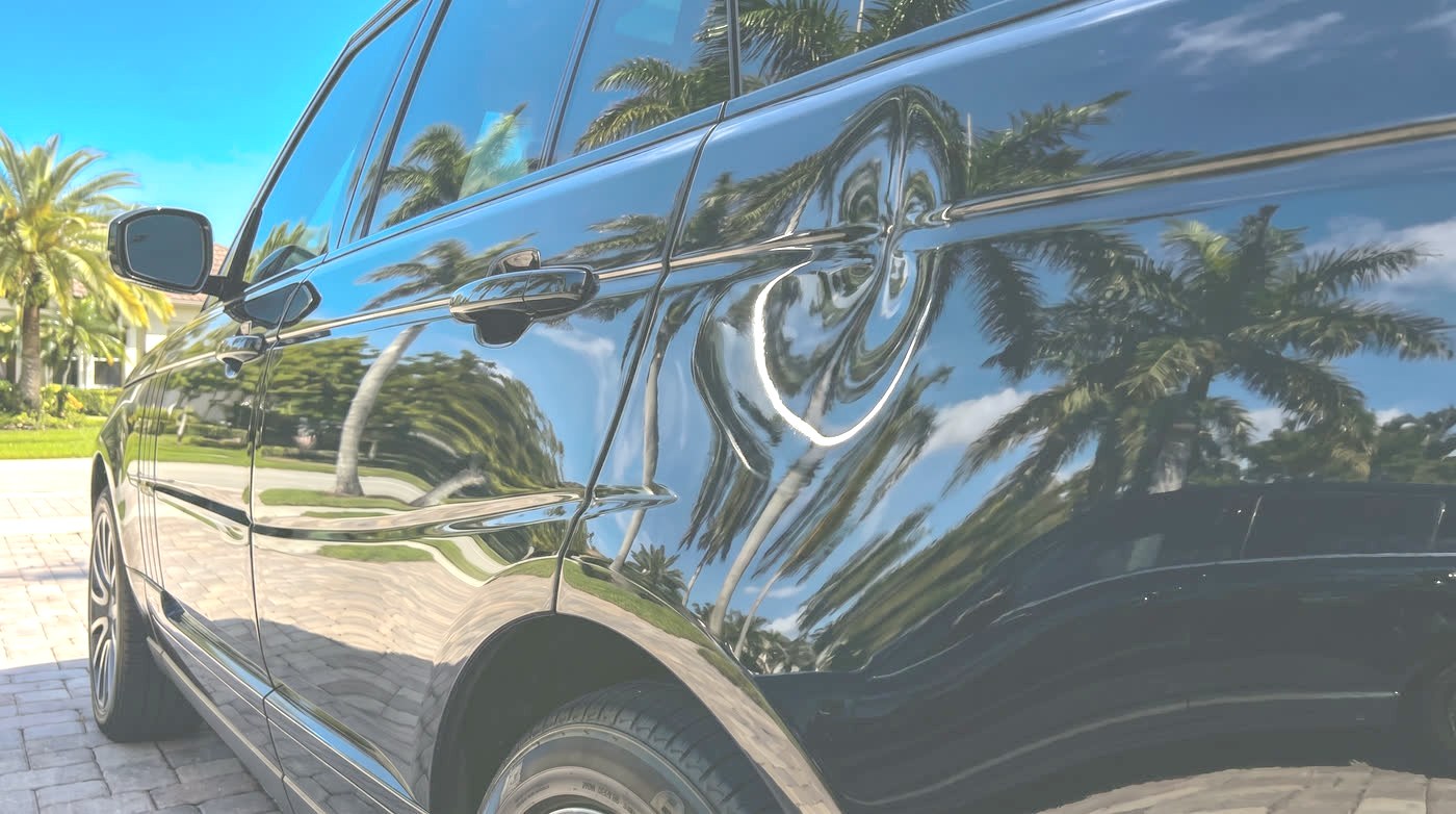 Before: a deep dent and a long crease in the side of a black luxury SUV, warping the palm tree reflections.