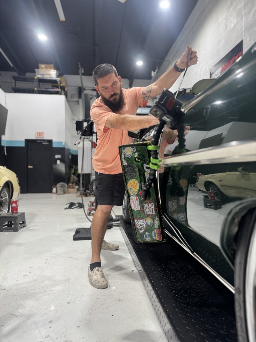 A Gold Coast PDR technician reading the reflection on a dark green classic through an LED line board, rod in hand behind the panel.